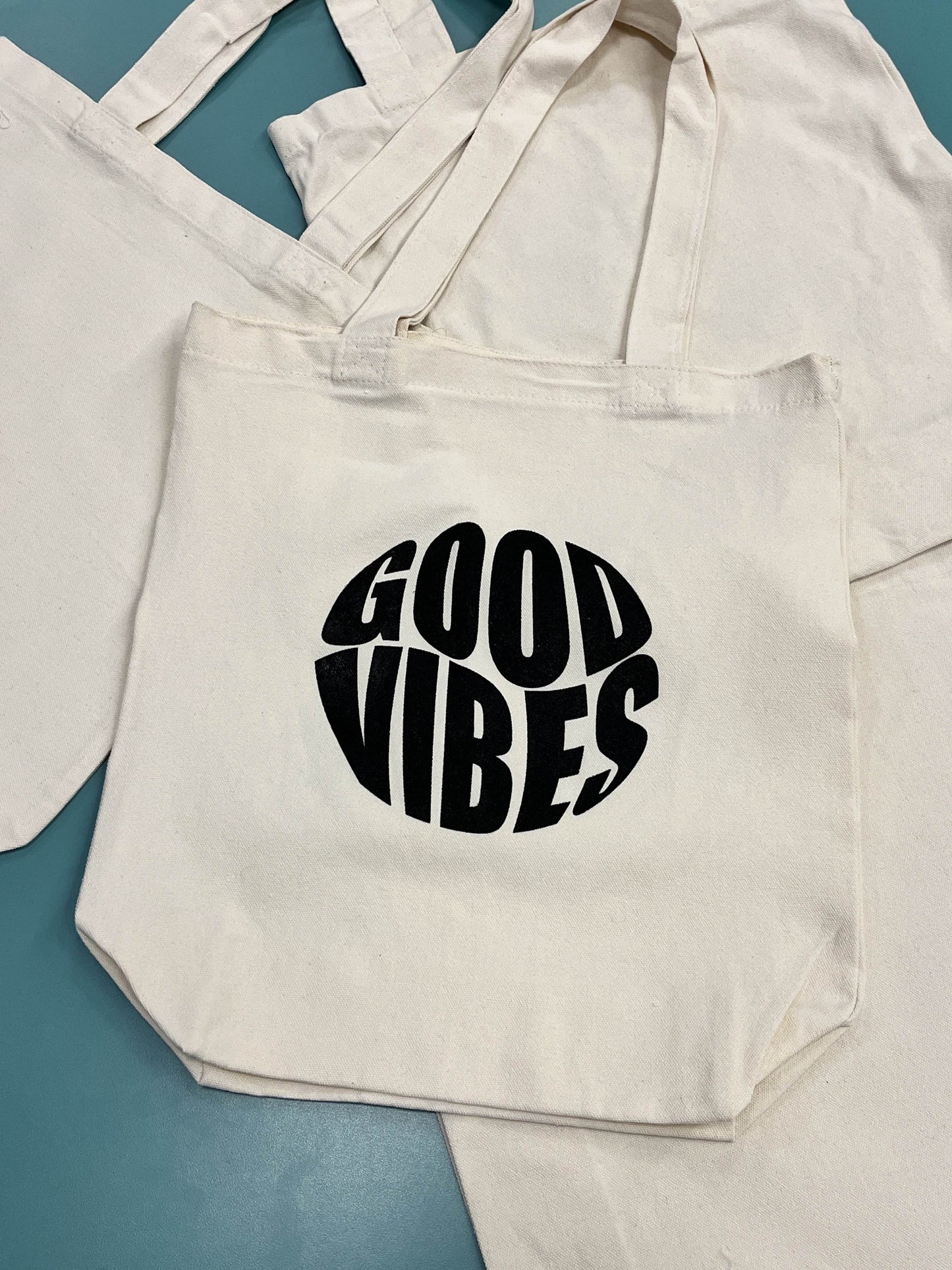 Beige tote bag with 'Good Vibes' text on a blue surface